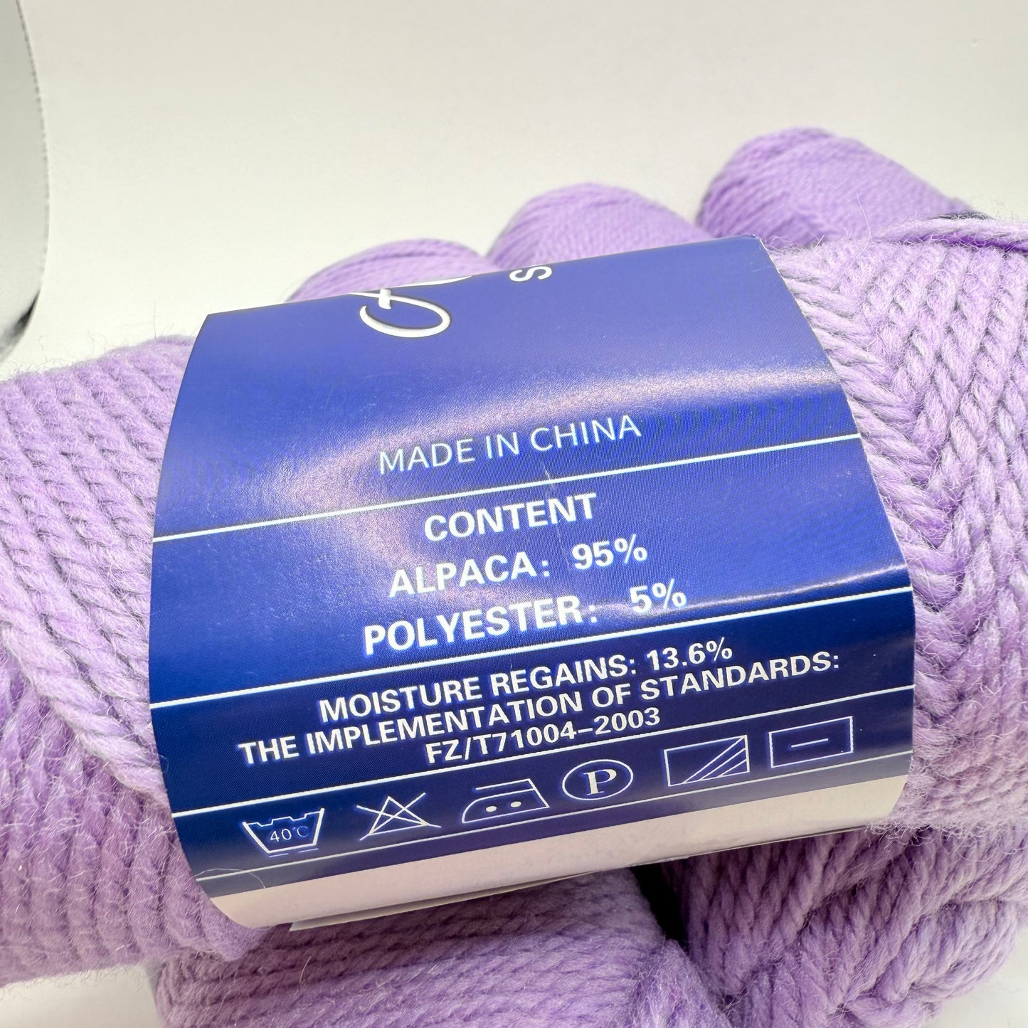 A skein of light purple yarn, 95% alpaca and 5% polyester, with care instructions.