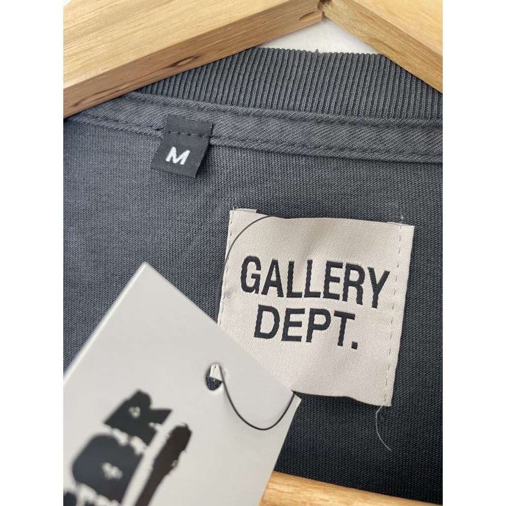Gray shirt with a "Gallery Dept." tag and size "M" label, hanging on a wooden hanger.