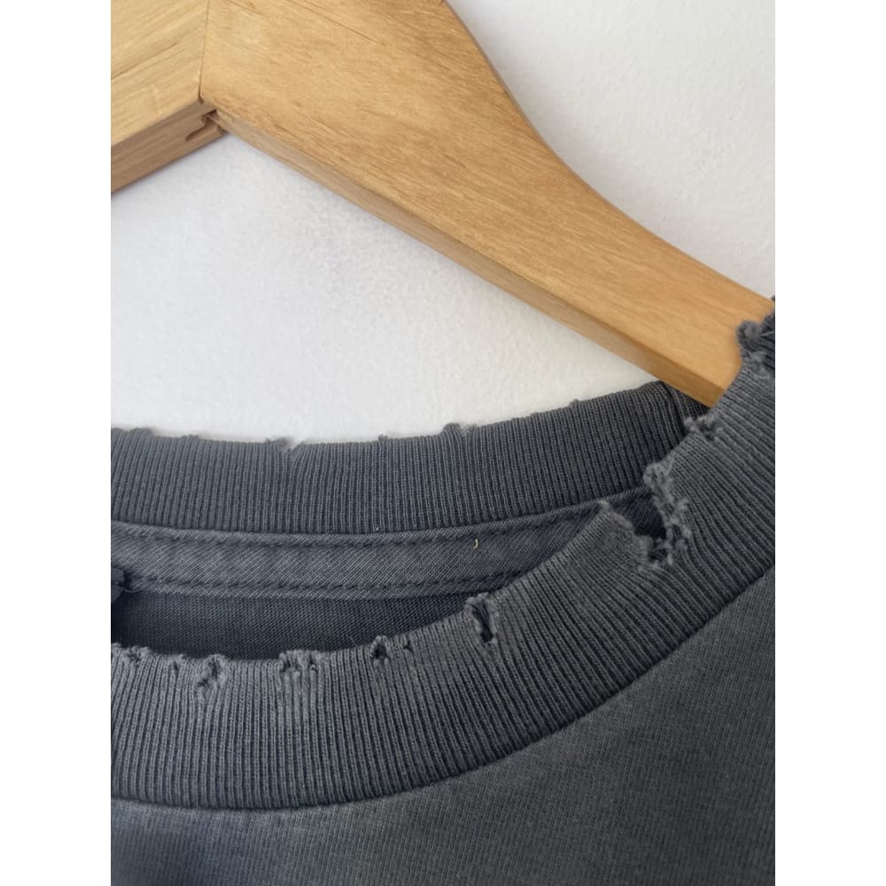 Close-up of a gray t-shirt with a ripped neckline, hanging on a wooden hanger.