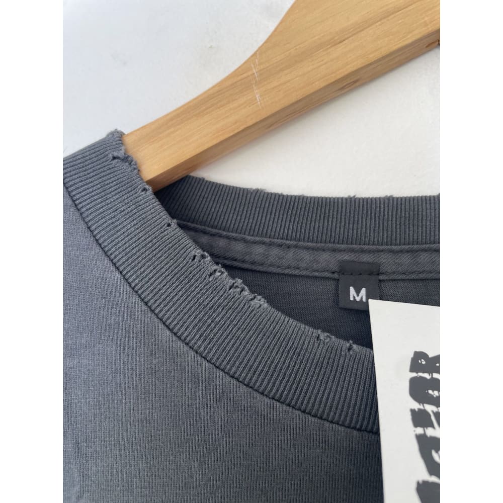 Close-up of a gray t-shirt with a ribbed collar on a wooden hanger. A tag is visible below the collar.