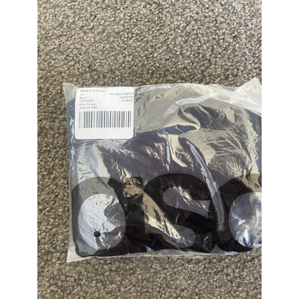 Sealed black Asos Design garment in plastic packaging on carpet.