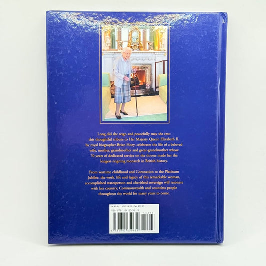 A hardcover book with a dark blue cover featuring a central image of Queen Elizabeth II and descriptive text.