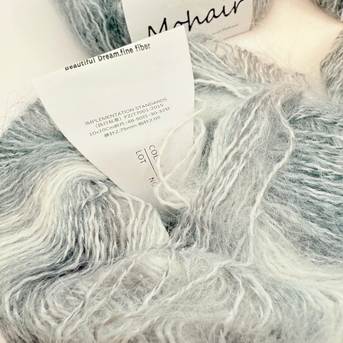 A skein of soft, fluffy mohair yarn in shades of grey and white.