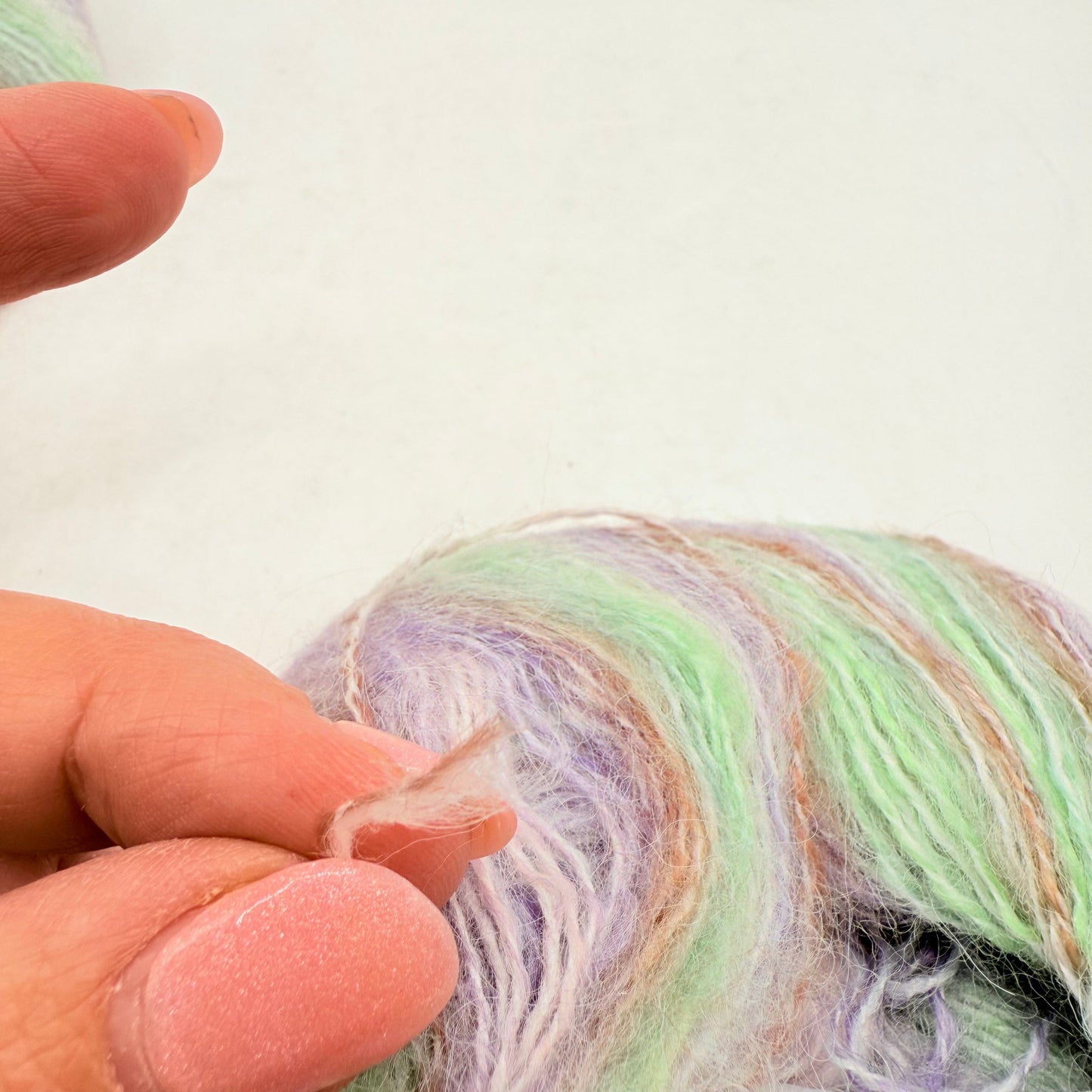 A personās hand holding a small, translucent piece of plastic near a skein of pastel-colored yarn.