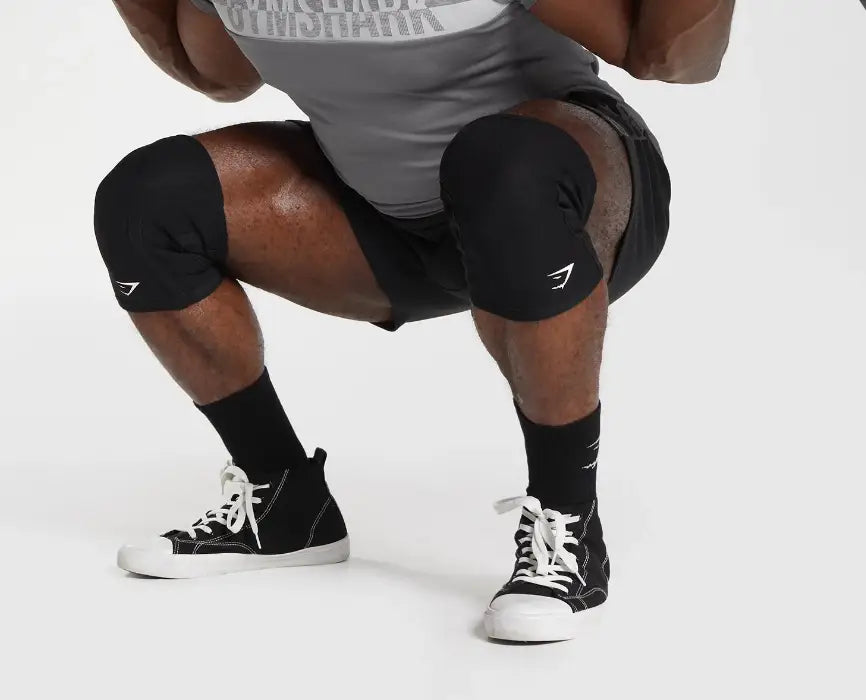 A person wearing black knee sleeves and high-top sneakers while squatting.