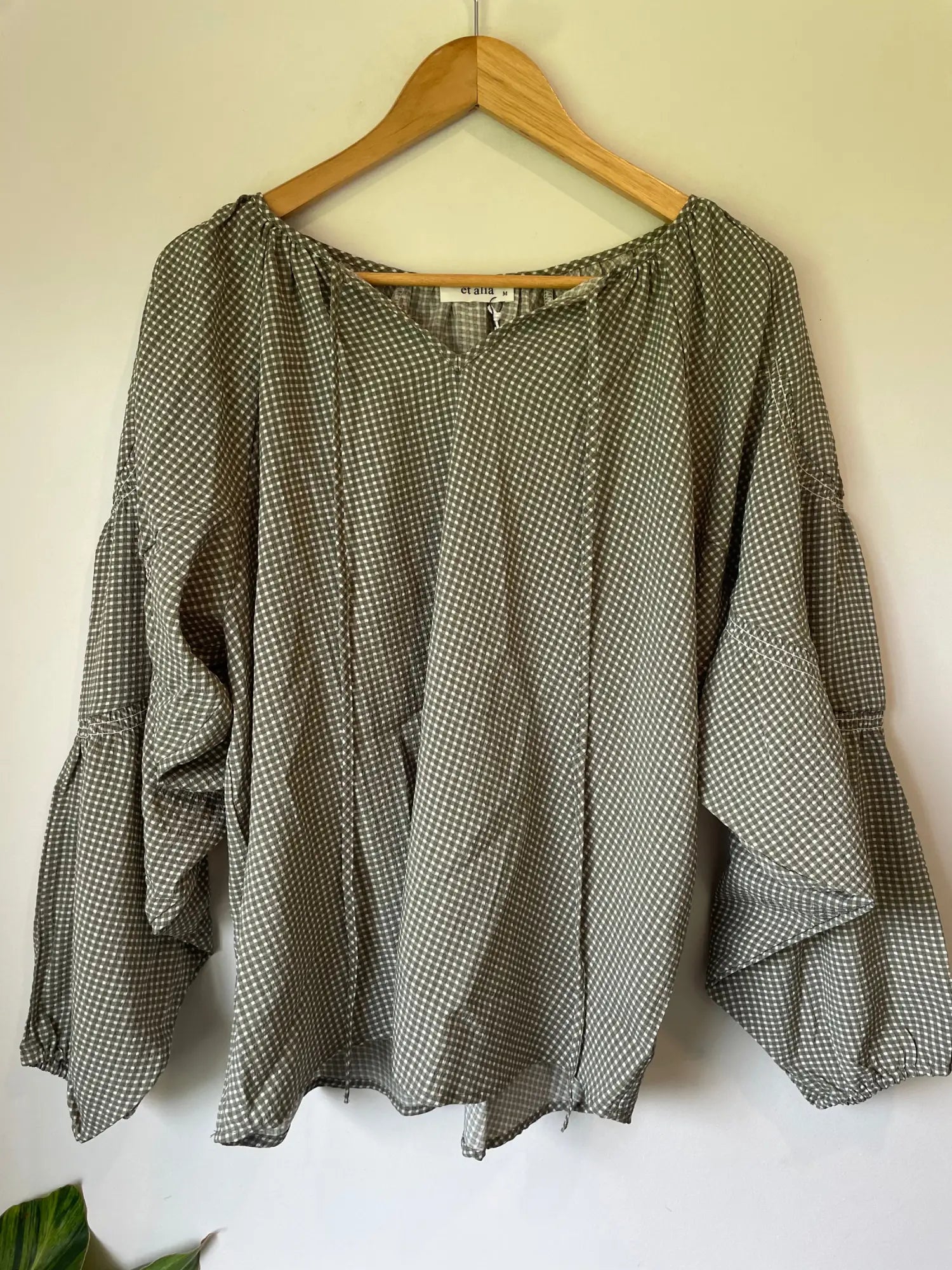 A loose-fitting, long-sleeved blouse with a small pattern of light dots on a dark background, featuring a V-neck with ties and gathered cuffs.