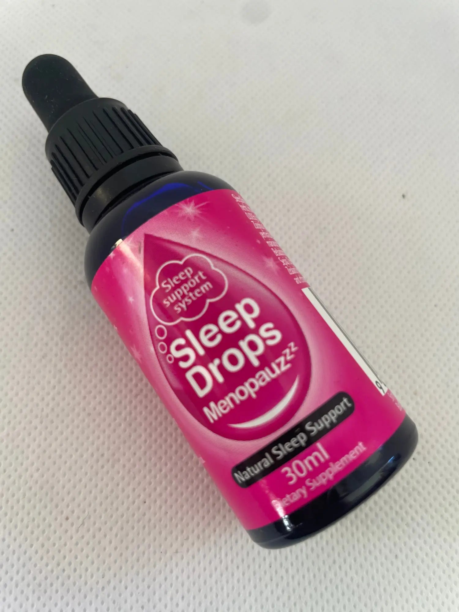 A dark blue glass dropper bottle with a pink label for ’Sleep Drops Menopauzz’, a natural sleep support dietary supplement.