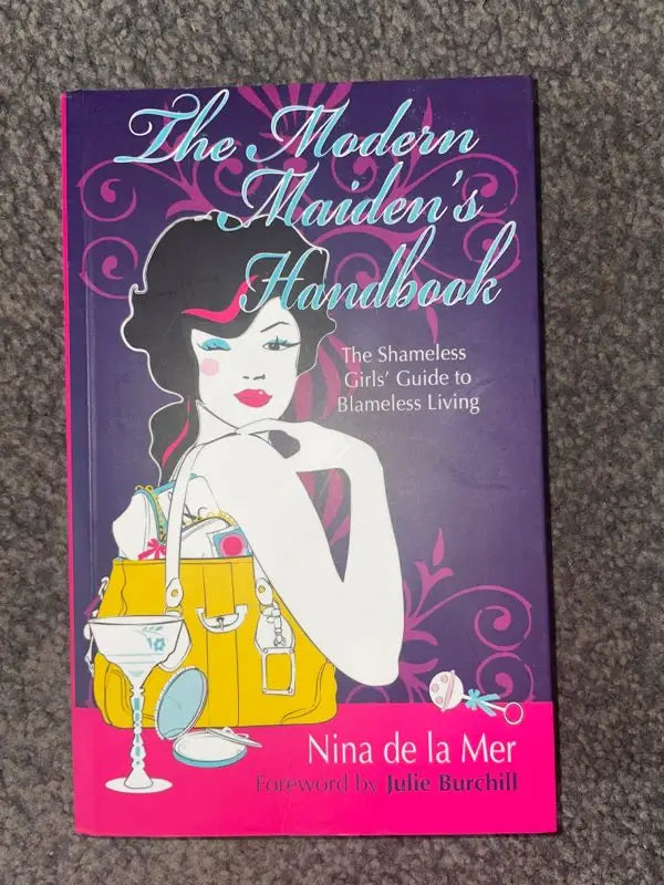 A book titled ’The Modern Maiden’s Handbook’ with a vibrant purple and pink cover featuring an illustrated woman.