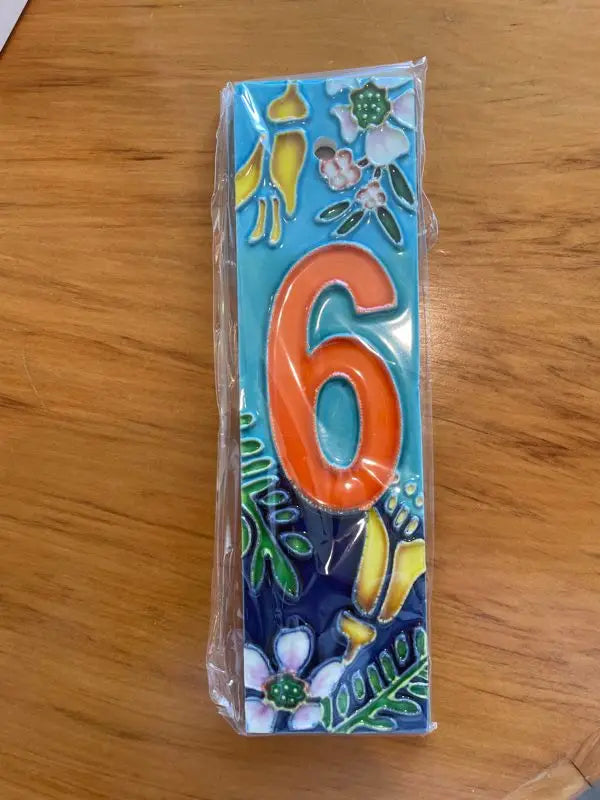Rectangular decorative house number tile with a prominent orange ’6’’ and floral motifs.