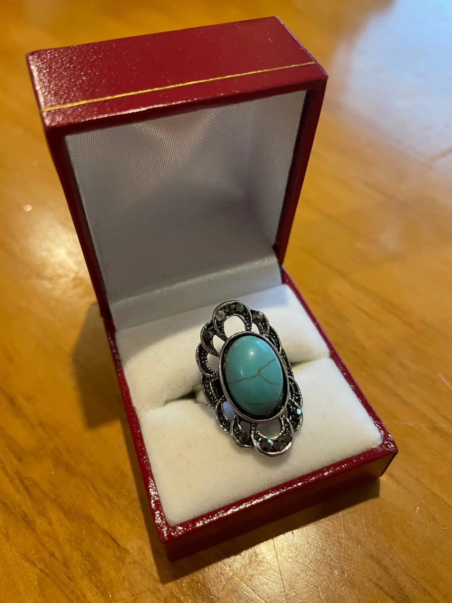 An ornate silver ring with an oval turquoise stone in a red ring box.