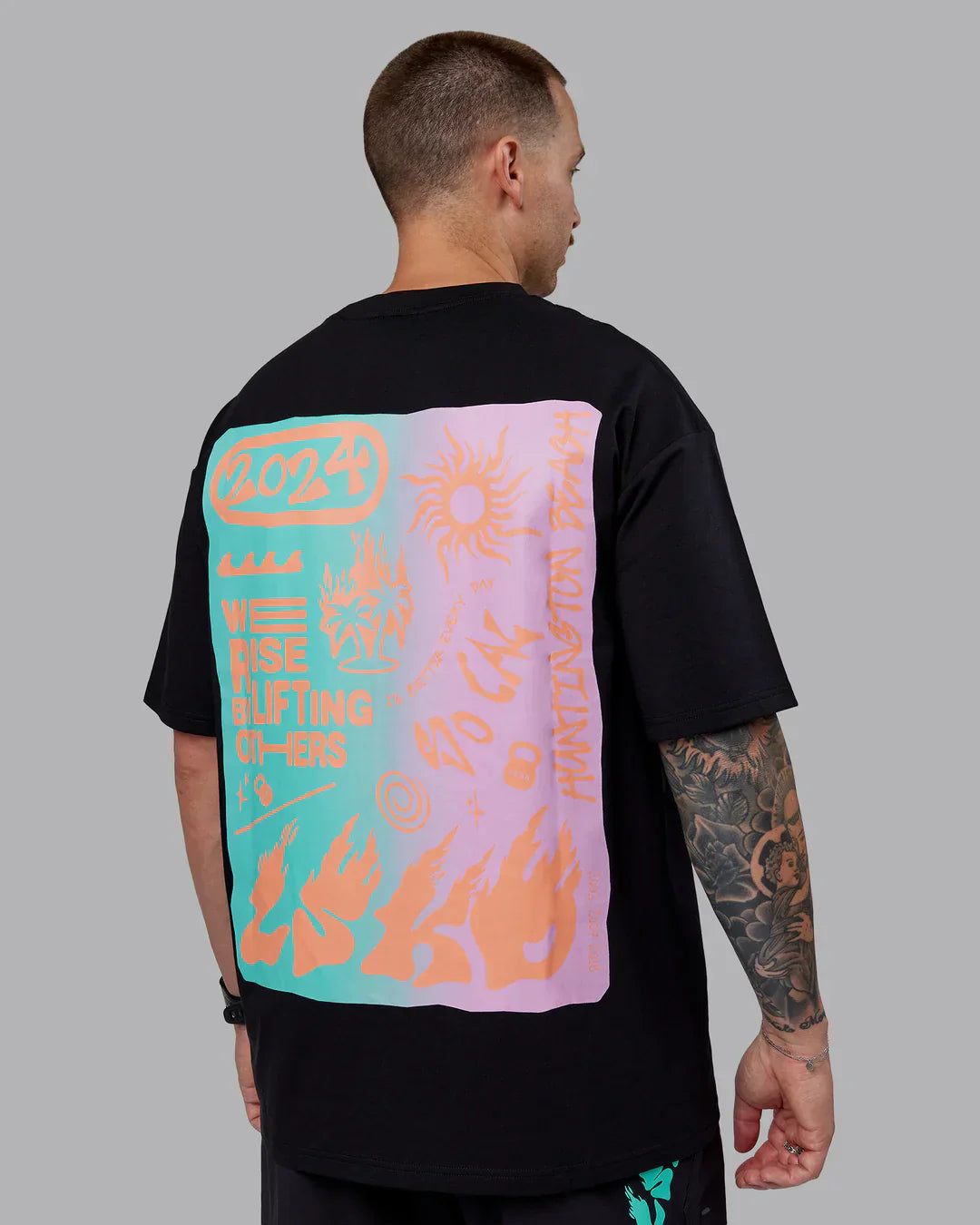 A black oversized t-shirt with a large rectangular graphic print on the back featuring a gradient of teal to pink, adorned with orange flame-like designs and various abstract symbols.