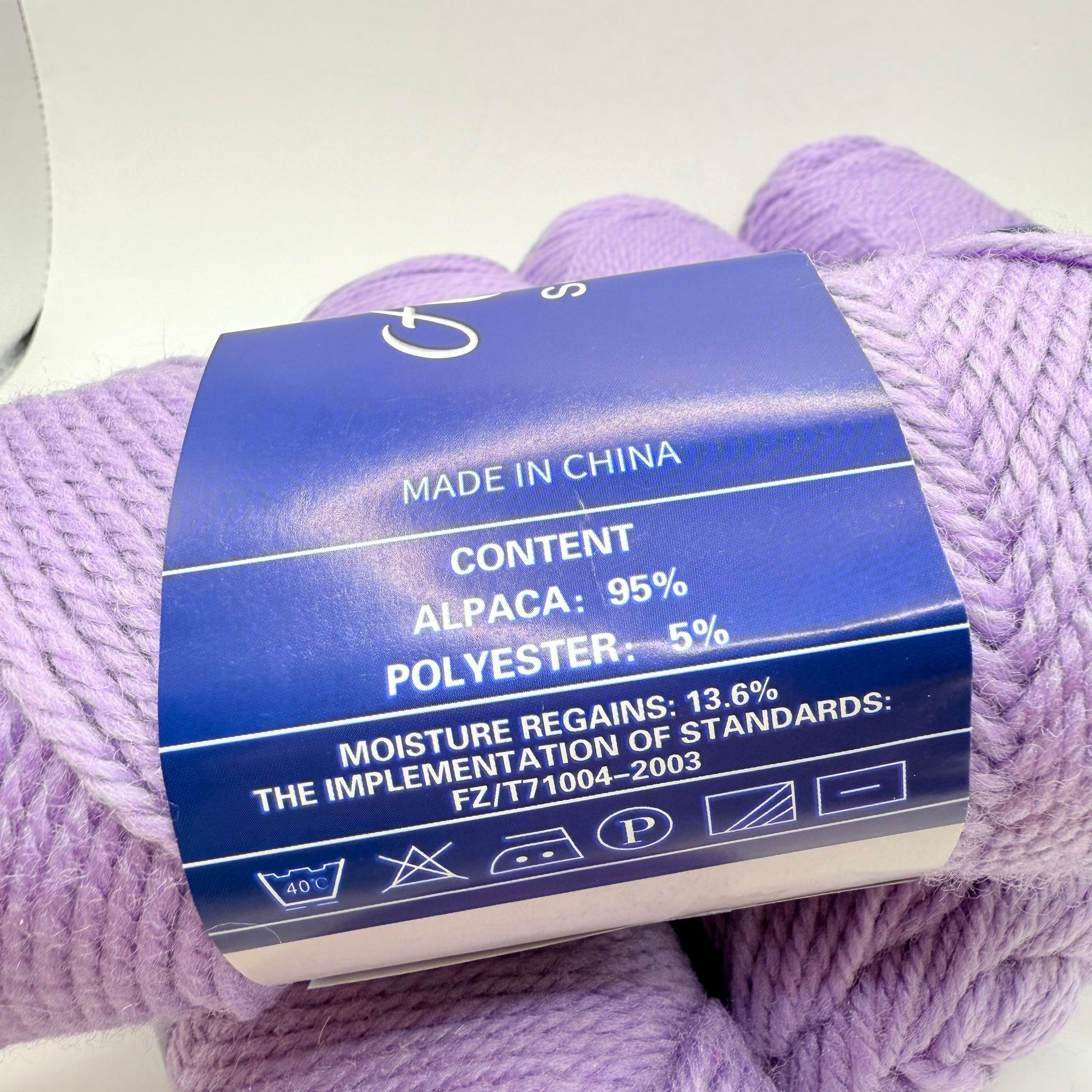 A skein of light purple yarn, 95% alpaca and 5% polyester, with care instructions.