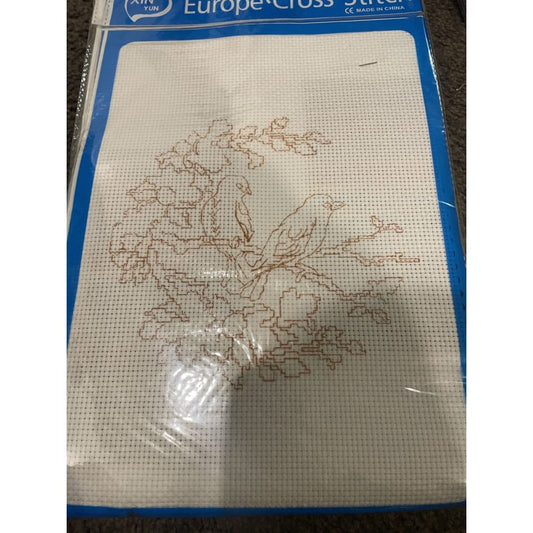 Cross-stitch kit featuring two birds on branches, printed on white aida cloth with blue packaging.
