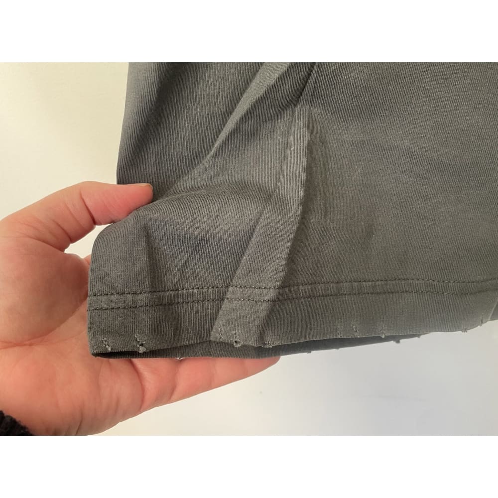 Close up of a grey t-shirt with frayed edges held by a person's hand.
