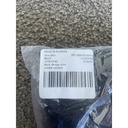 Product tag in plastic wrap. The tag is labeled "MADE IN ALBANIA", "One Size", "Black", "Asos design m+m crinkle ruched", and also includes a barcode and several numbers.