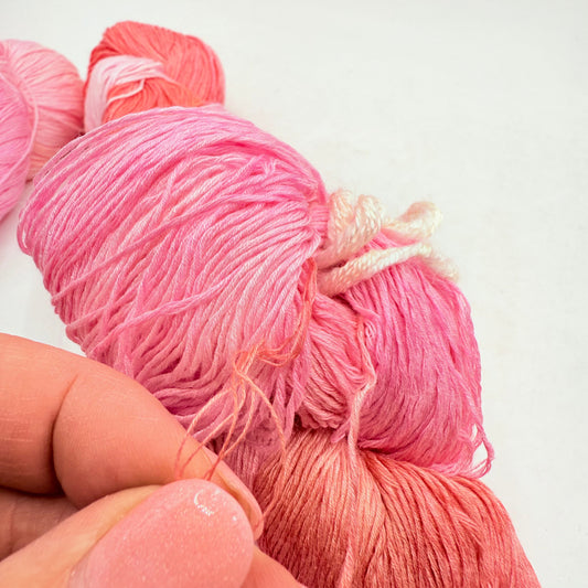 A person’s hand holding several skeins of pink and coral ombré yarn.