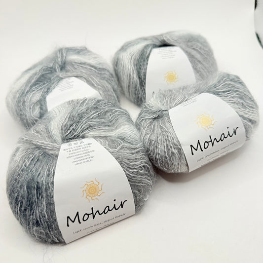 Four skeins of soft, fluffy gray and white variegated mohair yarn.