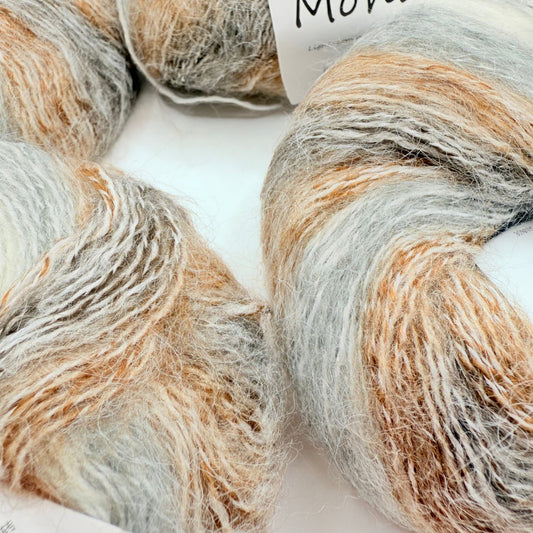 Several skeins of soft, fluffy yarn in shades of light grey, white, and warm browns.