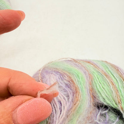 A person’s hand holding a small, translucent piece of plastic near a skein of pastel-colored yarn.